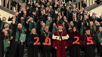 Absolwenci stoją na schodach w uroczystych strojach i rzucają biretami