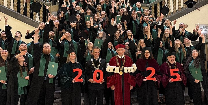 Absolwenci stoją na schodach w uroczystych strojach i rzucają biretami