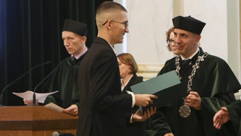 Dziekan w todze wręcza studentowi w garniturze akt immatrykulacji