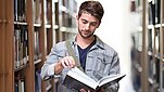 Student z książką na tle regałów z książkami