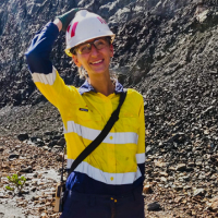 Uśmiechnięta kobieta w kamizelce i kasku stojącej w kopalni odkrywkowej. Zdjęcie profilowe.