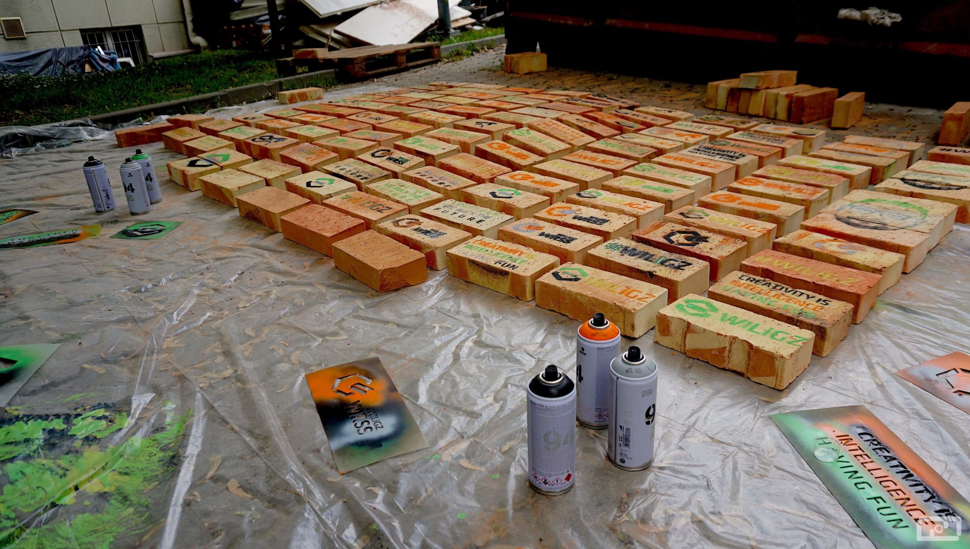 Pomalowane cegły leżące na foli malarskiej. Przed nimi leży szablon z logiem WRSS.