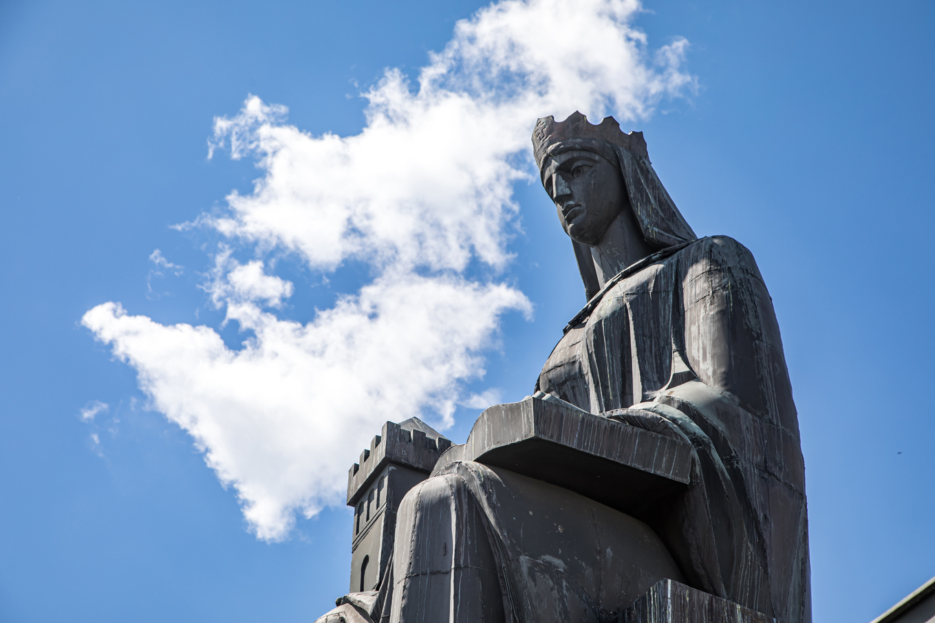 Pomnik świętej Barbary na tle błękitnego nieba oraz białej chmury. Ujęcie od dołu.