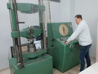 Pracownik obsługuje zieloną maszynę do ściskania z metalowym pokrętłem.