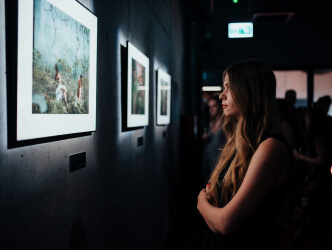 Młoda kobieta obserwuje zawieszony obraz na szarej ścianie.
