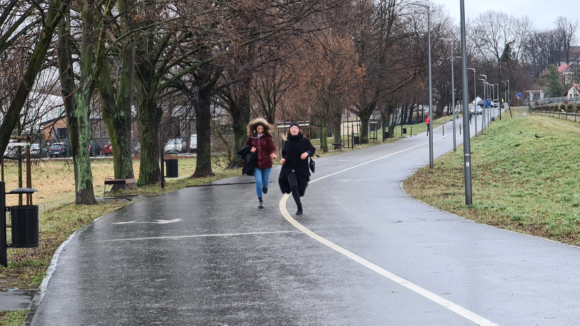 Dwie kobiety w kurtkach i płaszczach biegną po ulicy