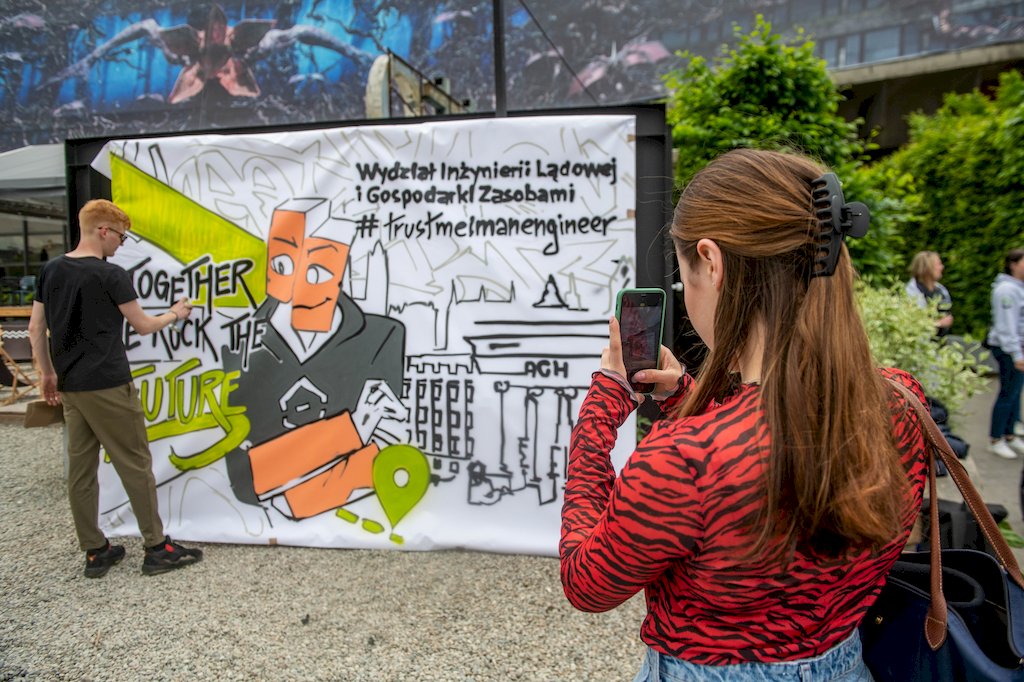 Studentka robi zdjęcie telefonem malującemu graffiti studentowi