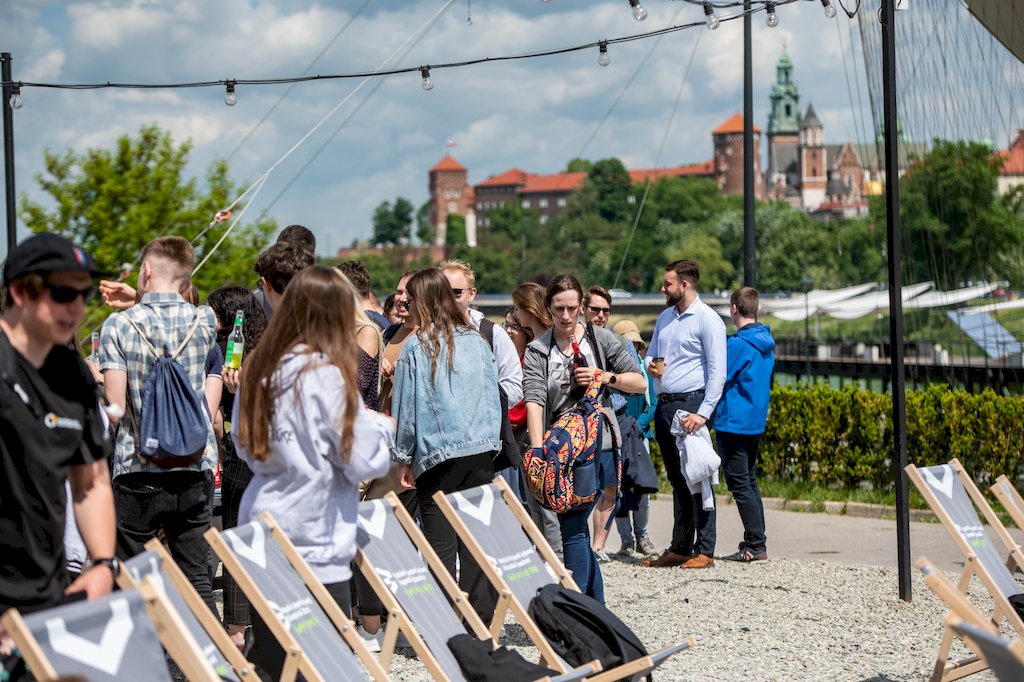 Studenci stoją przy szarych leżakach z napisem Wydział Inżynierii Lądowej i Gospodarki Zasobami. W tle Zamek na Wawelu.