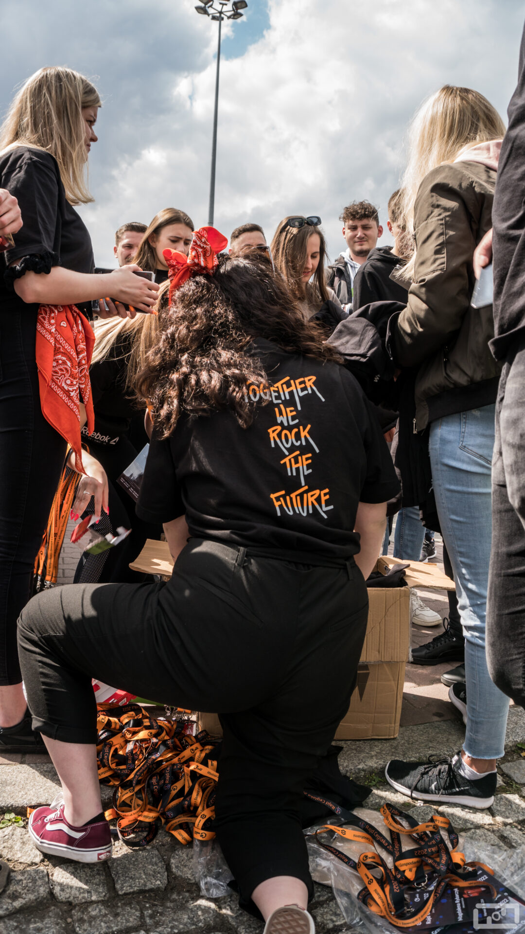 Rozmawiający ze sobą. W centralnej cześci zdjęcia znajduje się studnetka obrócona tyłem, która ubrana jest w czarną bluzę z pomarańczowo szarym napisem: Together we rock the future.