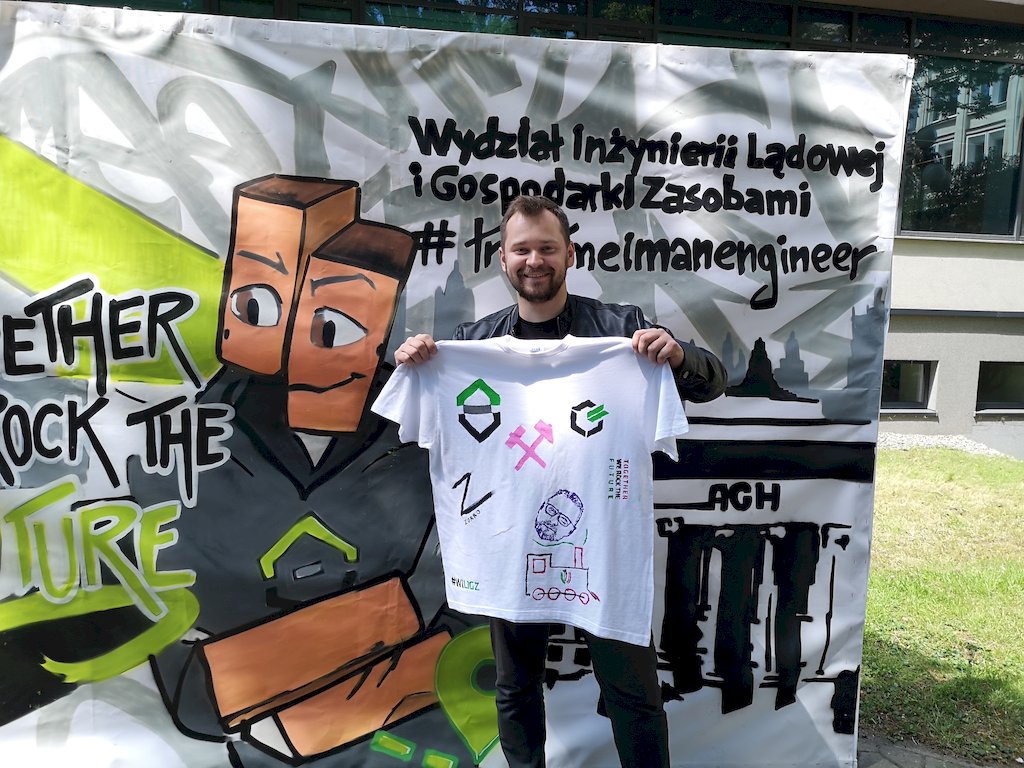 Student prezentuje koszulkę z namalowanymi różnymi logotypamia WILIGZ, WRSS WILiGZ, młotkami górniczymi, lokomotywą.