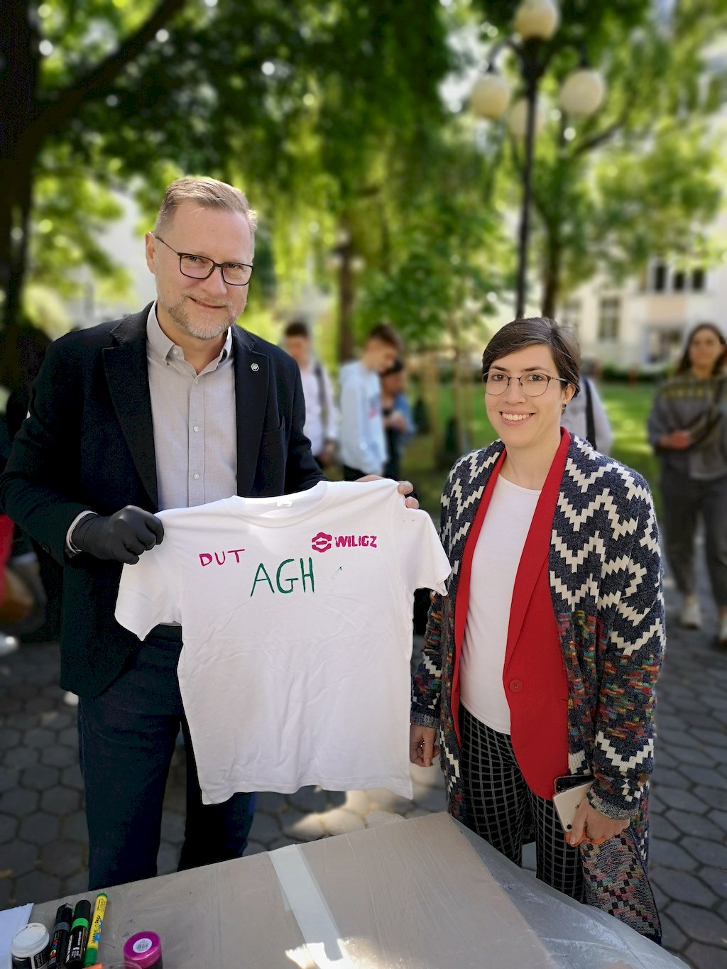 Dziekan prof. Marek Cała prezentuje białą koszulkę z namalowanym napisem AGH WILGZ DUT stojąc obok kobiety w okularach, która ją namalowała.