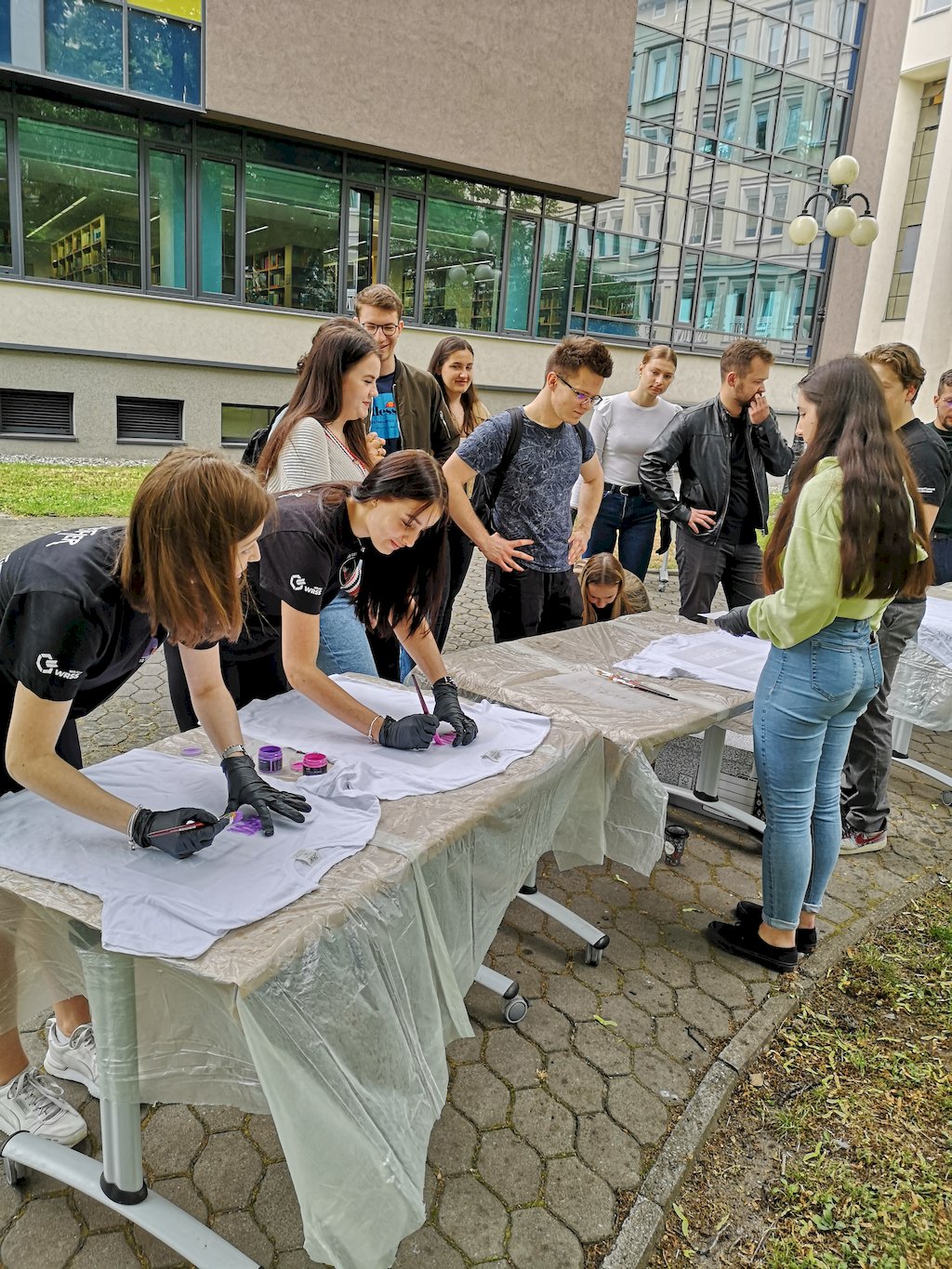 studentki i studenci malują koszulki na stołach