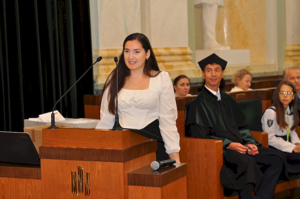 Młoda uśmiechnięta kobieta w białej bluzce stoi na mównicy