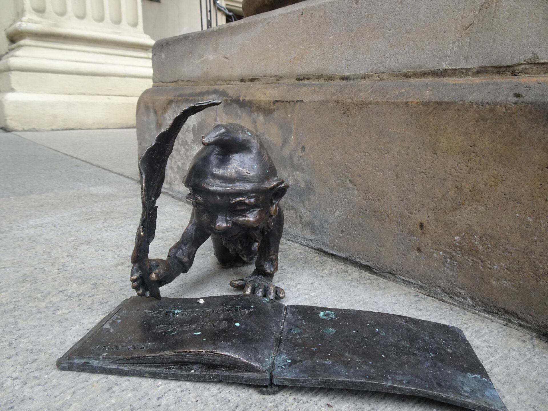 Rzeźba wykonana z brązu. Rzeźba przedstawia wrocławskiego skrzarta który pisze gęsim piórem po książce. Rzeźba jest na chodniku.