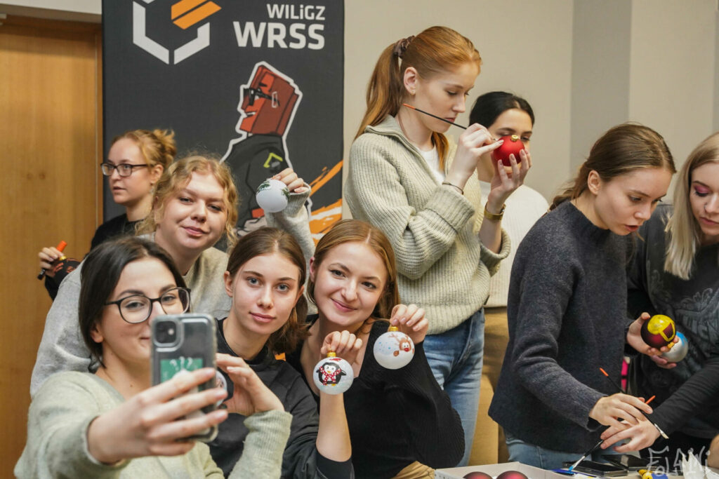 Na zdjęciu widać studentki i studentów WILiGZ malujących kolorowe bombki. W tle widać baner z napisem WRSS.